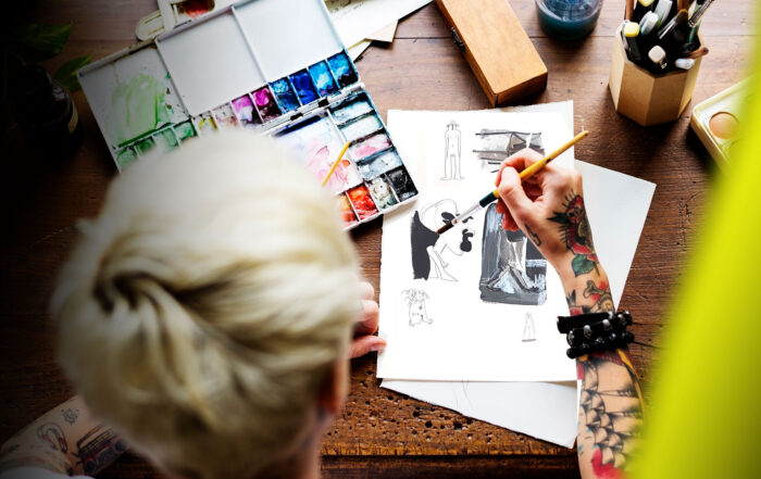 Person mit tätowiertem Arm malt mit Aquarellfarben an Illustrationen für eine Kunstmappe