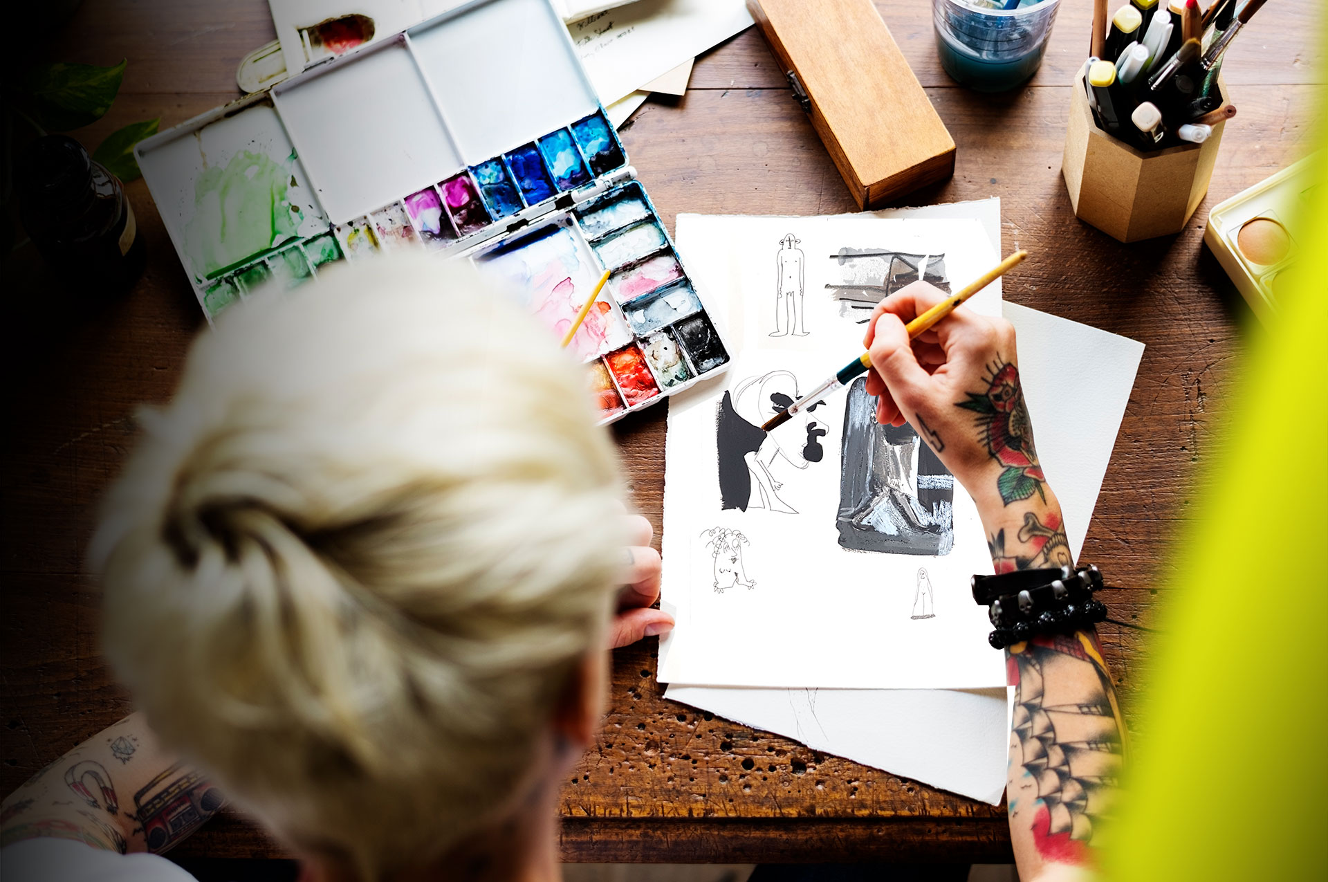 Person mit tätowiertem Arm malt mit Aquarellfarben an Illustrationen für eine Kunstmappe