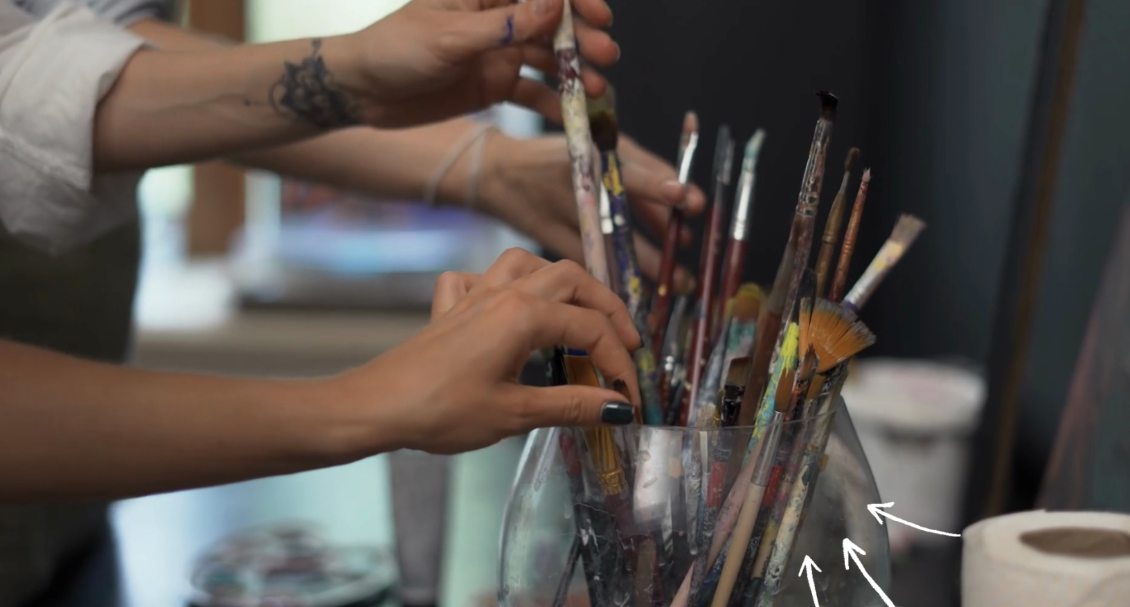 Ein großes Glas, in dem sich viele Pinsel befinden. Hände greifen danach.